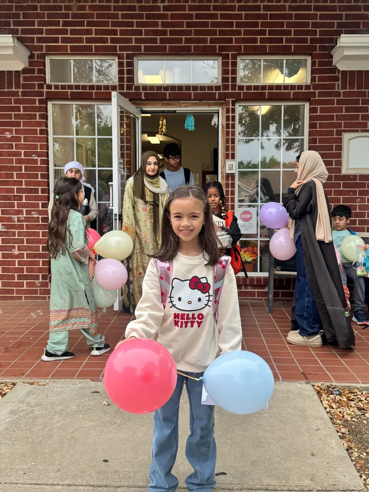 Children arriving at NAML Academy for a school event, with balloons at the entrance